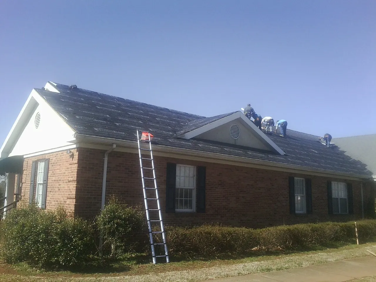 Crew tearing shingles off a brick ranch roof with a ladder set — Metal Roof Repair work by our crew in Odessa