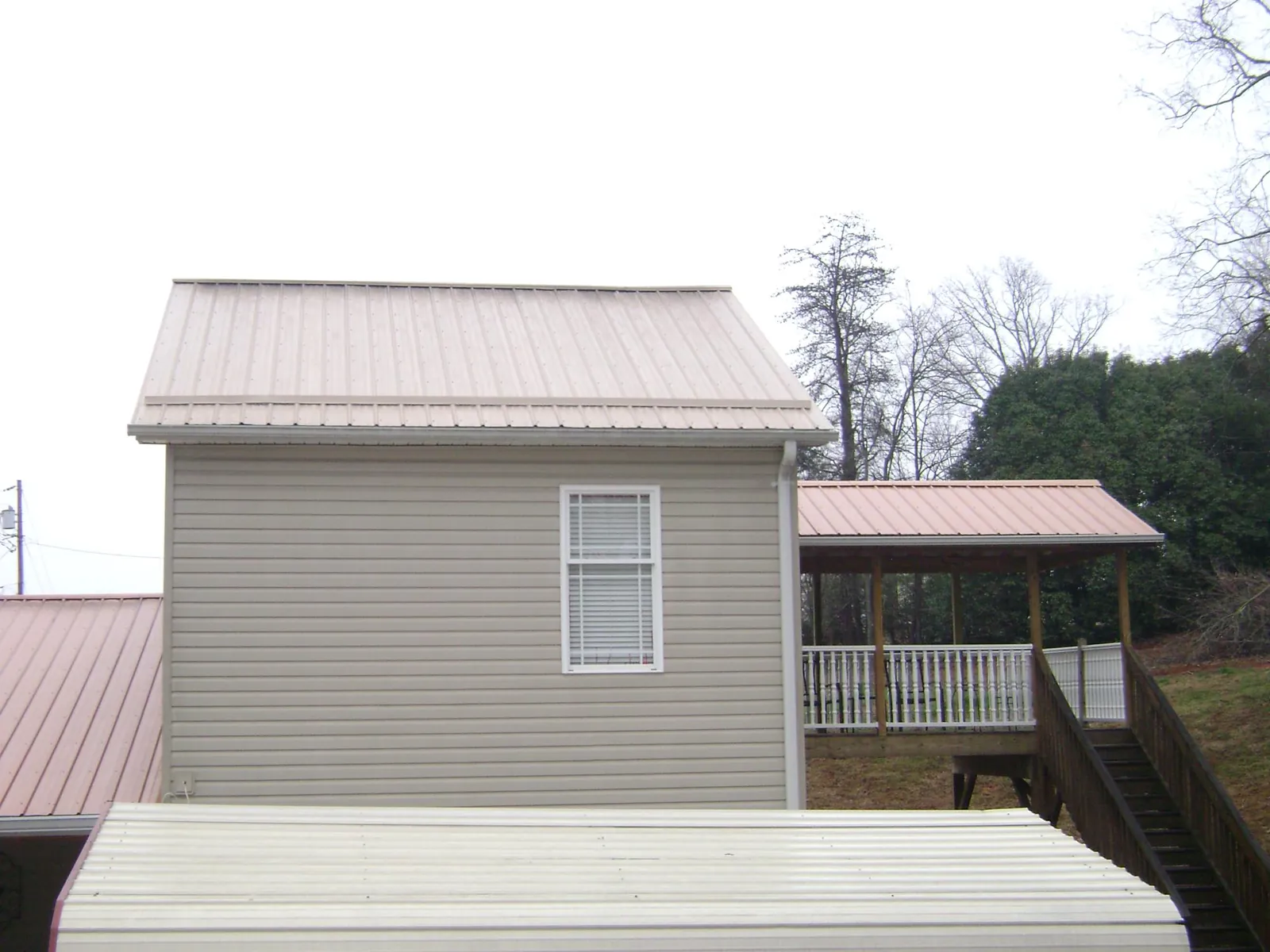 Tan metal roofs on a two story addition and attached porch, from a Roof Replacement job in Odessa